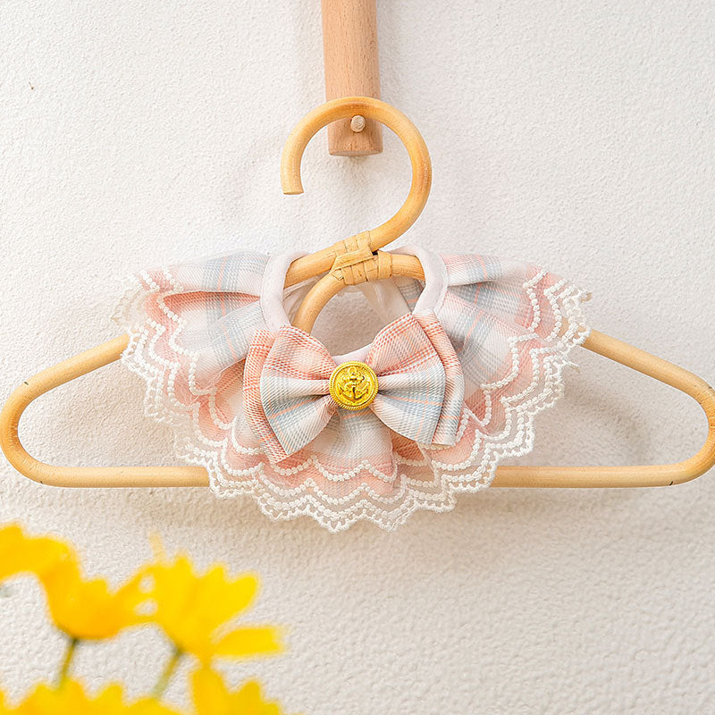 ​Collier de luxe pour chat en tissu rose poudré avec son petit nœud papillon et sa perle centrale, élégamment suspendu sur un cintre de présentation couture. Palais Félin Paris.