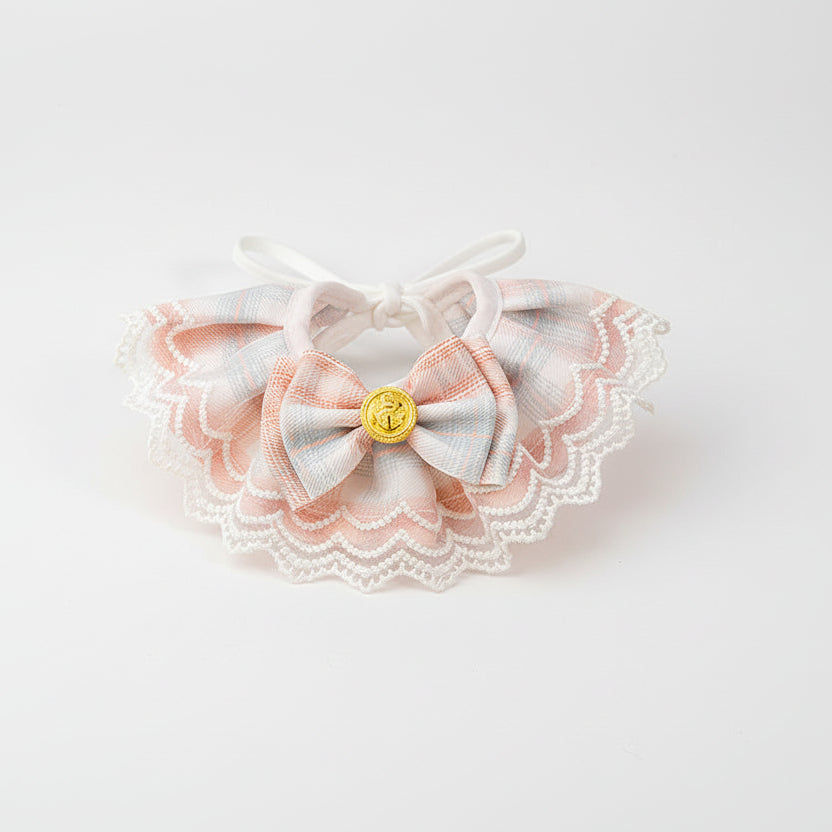 ​Collier de prestige pour chat en textile soyeux rose poudré, orné d'un nœud artisanal et d'une perle de nacre sur monture dorée - Palais Félin Paris.