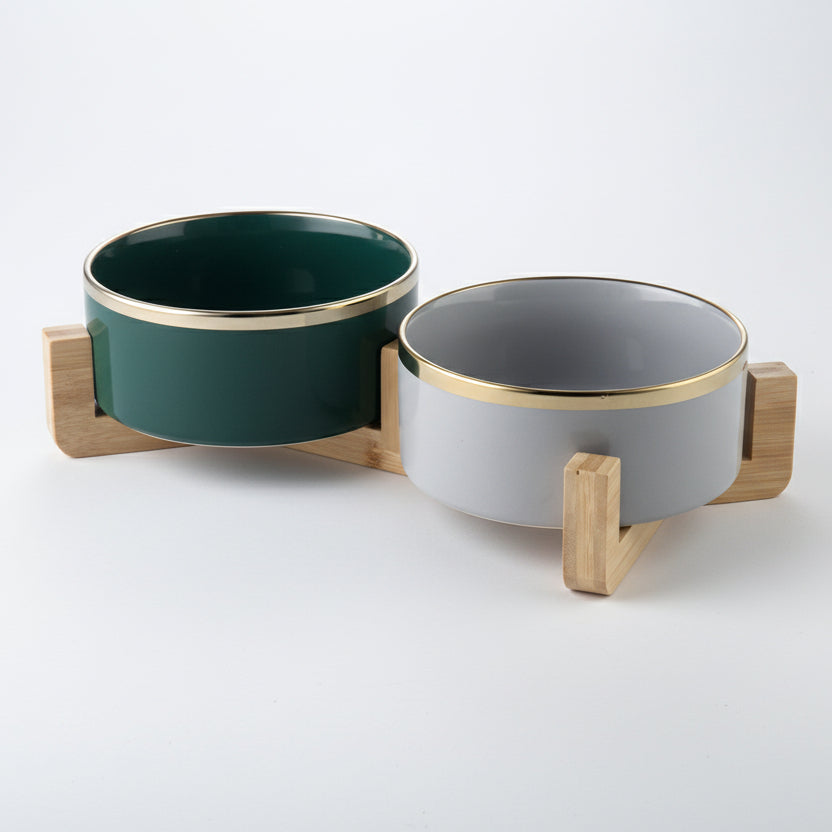 ​Ensemble duo de gamelles haut de gamme pour chat comprenant un bol en céramique noire et un bol en céramique blanche avec liserés dorés, sur un support minimaliste en bois clair, signée Palais Félin Paris.