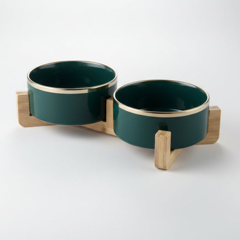 ​Ensemble de deux gamelles haut de gamme pour chat en céramique noire brillante avec liserés dorés élégants, surélevées par un support minimaliste en bois de chêne clair, signée Palais Félin Paris.