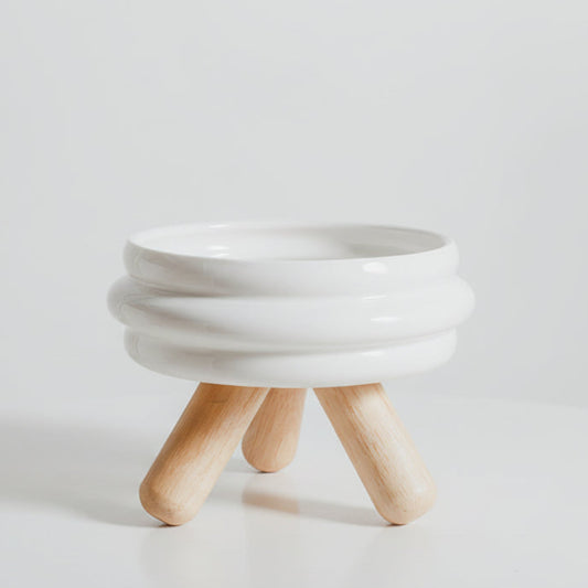 ​Gamelle individuelle au design épuré pour chat en céramique blanche monochrome, posée sur un support minimaliste en bois de chêne clair croisé, isolée sur un fond blanc, signée Palais Félin Paris.