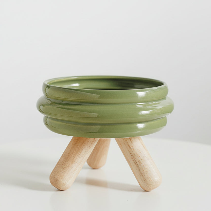 ​Gamelle individuelle au design contemporain pour chat en céramique verte, posée sur un support minimaliste en bois de chêne clair croisé, isolée sur un fond blanc, signée Palais Félin Paris.