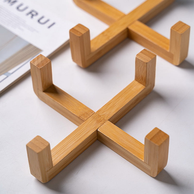 ​Support pour gamelle de chat en bois naturel de haute qualité, design en croix minimaliste et ergonomique posé sur une table blanche, Palais Félin Paris.